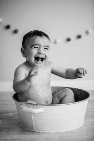 Baby boy giggles sitting in a tub as water pours over him