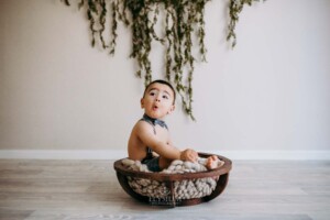 Baby boy pulls a funny face, sitting in a wooden bowl