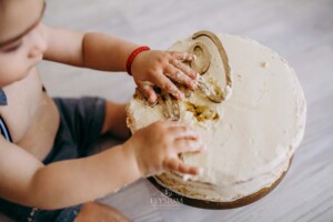 A little boy sits in front of his cake, touching the icing