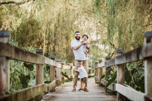 Family Photographer - A dad hugs his children as they stand on a boardwalk