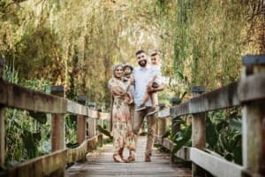 Family Photographer - A family stand cuddled together on a treelined boardwalk