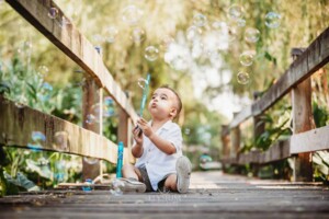 Family Photographer - A little boy sits on a boardwalk blowing bubbles