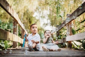 Family Photographer - 2 children sit on a boardwalk blowing bubbles