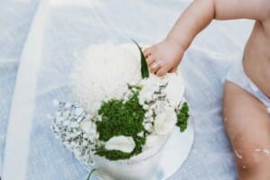 Family Photographer - A birthday cake, baby hand reaches out to touch the icing, cake smash session in Padstow