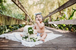 Family Photographer - A baby sits on a boardwalk tasting her birthday cake