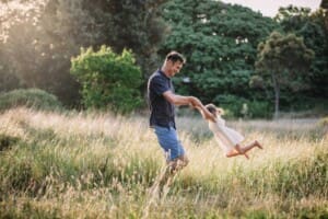 Family Photographer - A father swings his little girl around in a grass field