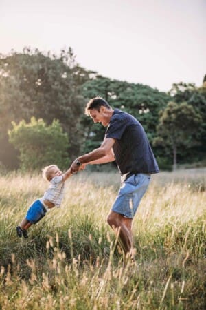 Family Photographer - A father spins his son around standing in grassy field