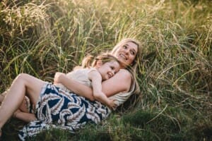 Family Photographer - a mother cuddles her daughter laying in long grass