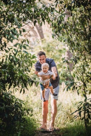Family Photographer - A dad swings his little boy as they stand in the bush