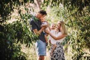 Family Photographer - Parents hug their children in green leafy field