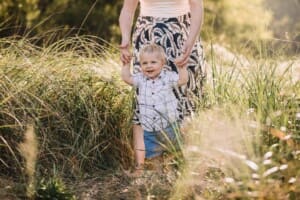 Family Photographer - A mother holds her baby boy's hands walking through long grass