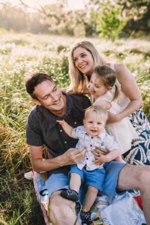 Family Photographer - A family sit in a grassy field cuddling at sunset