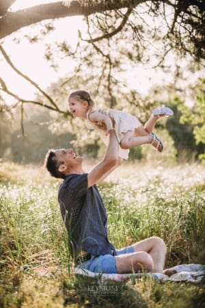 Family Photographer - A father hoists his daughter above him as she giggles