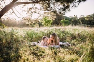 Family Photographer - A mum snuggles her little girl as they lay on a rug