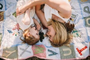 Family Photographer - A mum snuggles her little girl as they lay on a rug