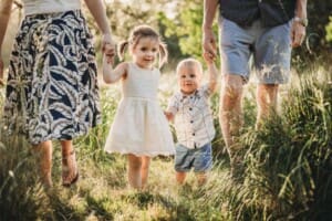 Family Photographer - Parents hold their children's hands walking in long grass