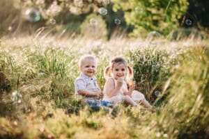 Family Photographer - children sit in long grass blowing bubbles
