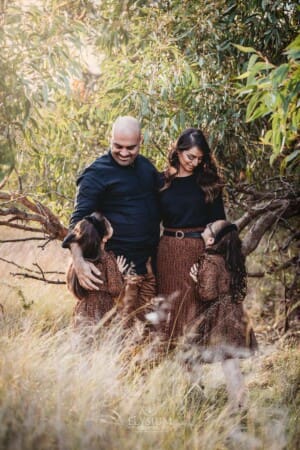 Family Photographer - A family stand in a grass field beneath a tree