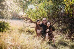 Family Photographer - A father hugs his little girls under a tree