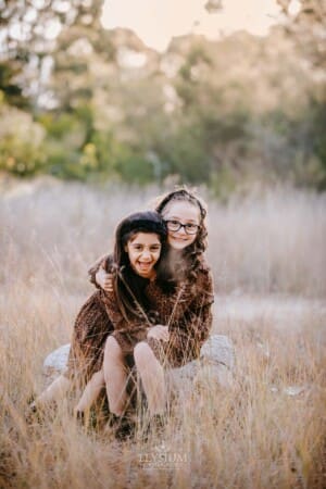 Family Photographer - Sisters hug each other and giggle at sunset
