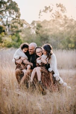 Family Photographer - Parents sit with their girls on their lap wrapped in a blanket