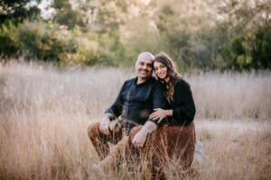 Family Photographer - A couple sit in a long grassy field at sunset