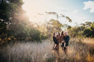 Family Photographer - parents hug their daughters as they stand in a grassy field