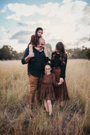 Family Photographer - A family stands in long grass and cuddle