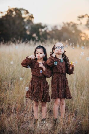 Family Photographer - girls blow bubbles standing in a grass field at sunset