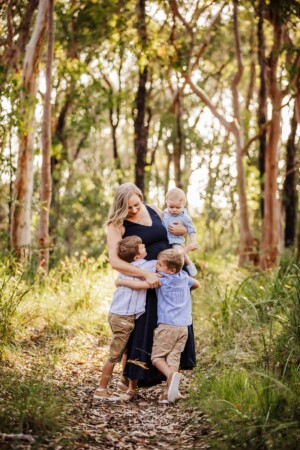 3 boys cuddle their mothers waist as they stand in Sydney bushland