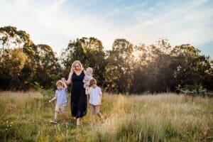 A mother and her sons walk hand in hand across a grass field at sunset