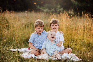 2 boys cuddle their baby brother as they sit in long grass