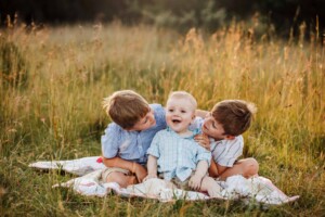 2 boys cuddle their baby brother as they sit in long grass