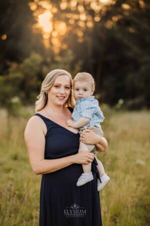 A mother cuddles her baby boy, grassy field at sunset