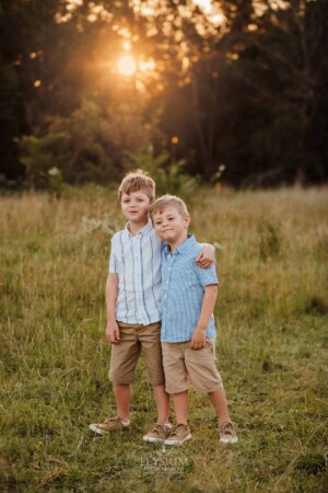 Brother stand in a sunlit grassy field, arms around each other
