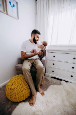 Newborn session - A dad sits in a chair and holds his baby girl in his arms