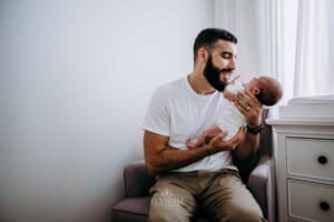 Newborn session - A father sits in an armchair and holds his baby girl