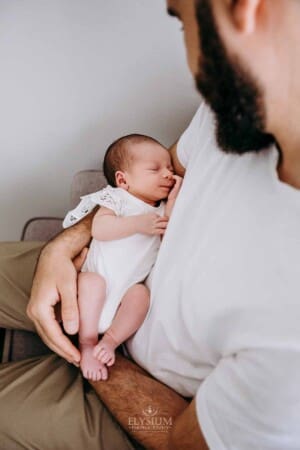 Newborn session - A father cradles his newborn daughter as they sit in a chair