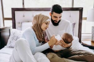 Newborn session - Parents look at their baby as they sit on a bed