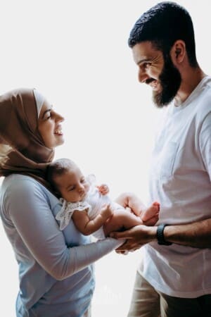 Newborn session - Parents stand in a bright window holding their baby