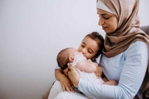 Newborn session - A little boy kisses his baby sister as they sit with their mum