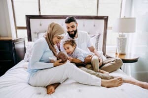 Newborn session - a family sit on a bed, little boy pats his baby sister