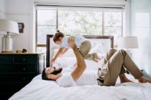 Newborn session - a father lifts his son above him as they lay on a bed