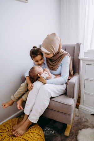 Newborn session - A little boy hugs his baby sister as they sit with their mum