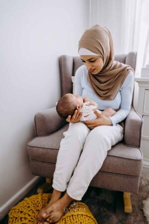 Newborn session - a mother sits in a chair, holding her baby girl in her arms