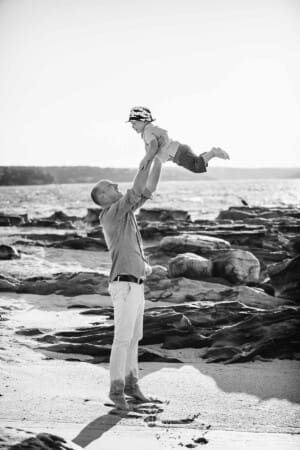 Maternity session - a dad lifts his son in the air, standing on a beach