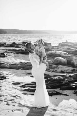Maternity session - pregnant mum hugs her son, standing on a sandy beach