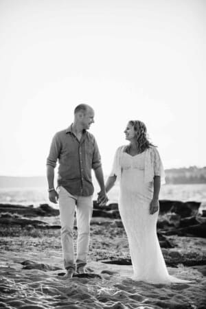 Maternity session - an expectant couple walk hand in hand along a beach