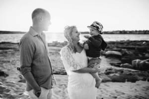 Maternity session - a family stand cuddling the pregnant mum on a beach at sunset