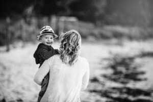 Maternity session - a little boy is carried by his pregnant mum walking on a beach